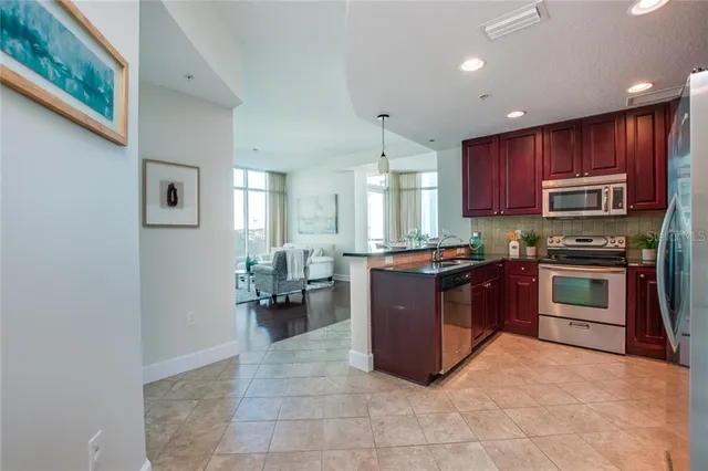 a large kitchen with stainless steel appliances granite countertop a stove refrigerator and a view of living room