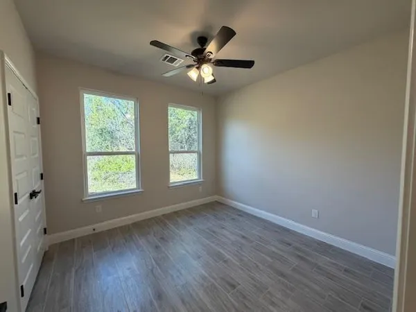 an empty room with wooden floor fan and windows