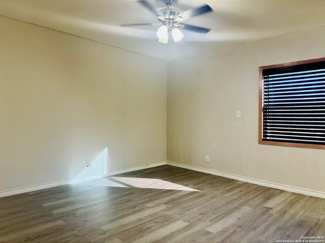 a view of an empty room with wooden floor and a ceiling fan