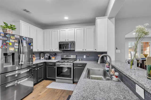 a kitchen with stainless steel appliances granite countertop a stove top oven a sink dishwasher and a refrigerator with wooden cabinets