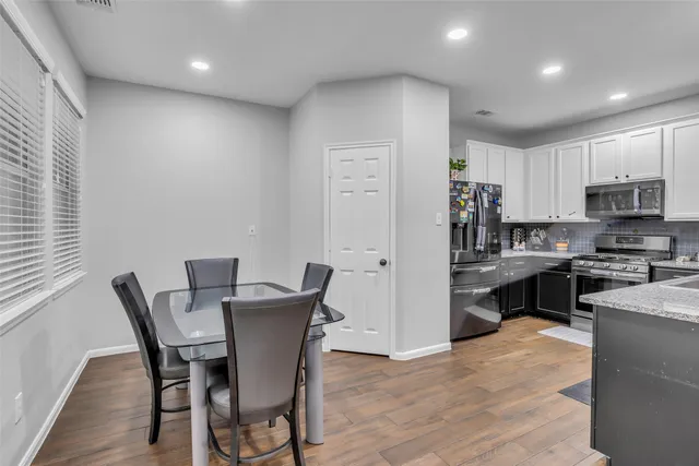 a kitchen with stainless steel appliances granite countertop a refrigerator a stove top oven a sink dishwasher and a dining table with wooden floor