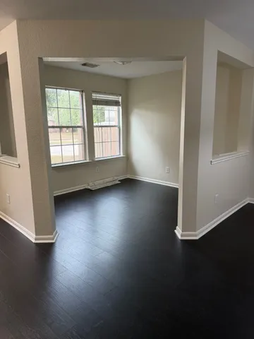 an empty room with wooden floor and windows with curtains