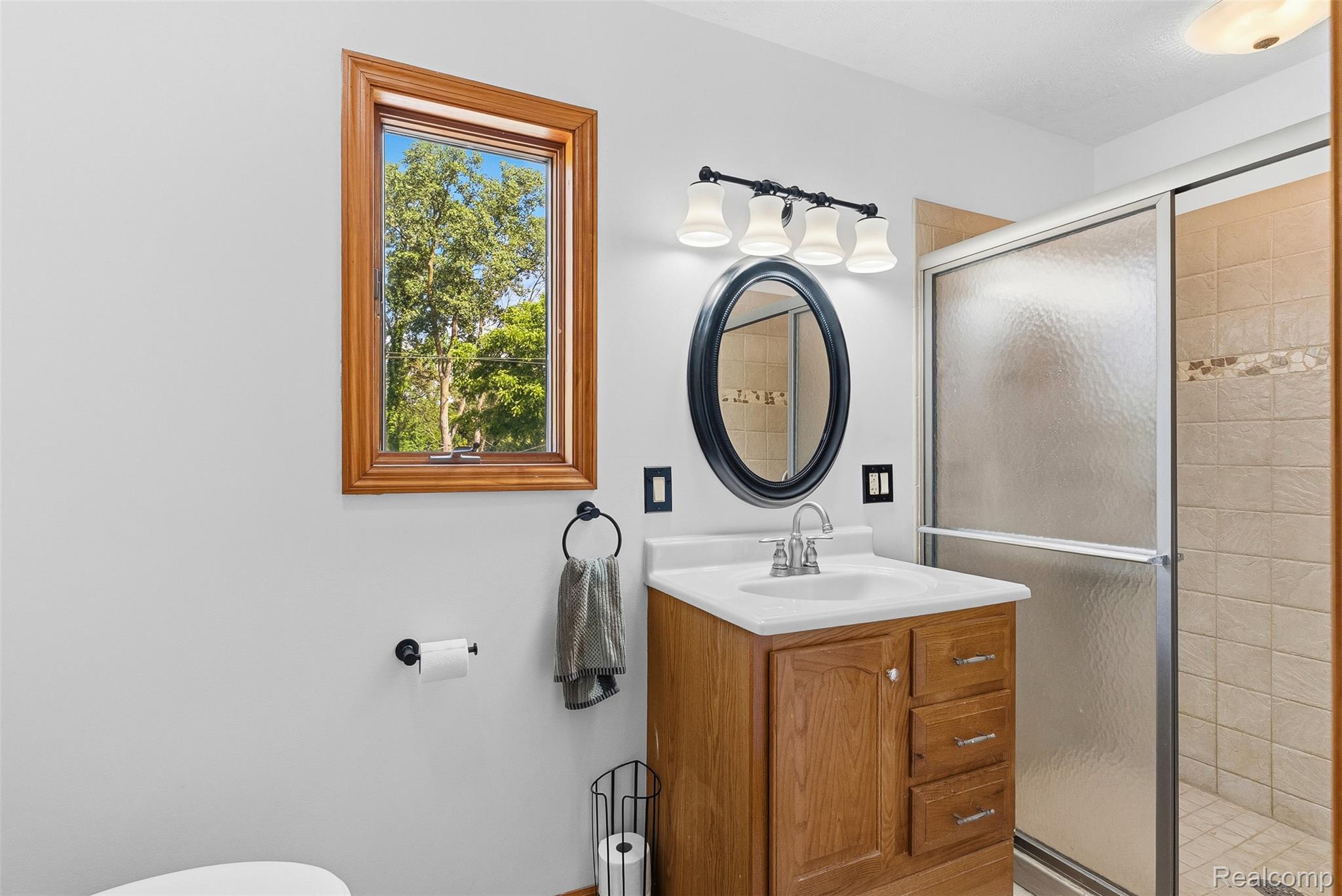 6699 Lansing Road Durand, MI 48429 - Photo 29 of 53 Bathroom featuring a wood-finish vanity with an integrated sink, an oval framed mirror, and a four-light fixture