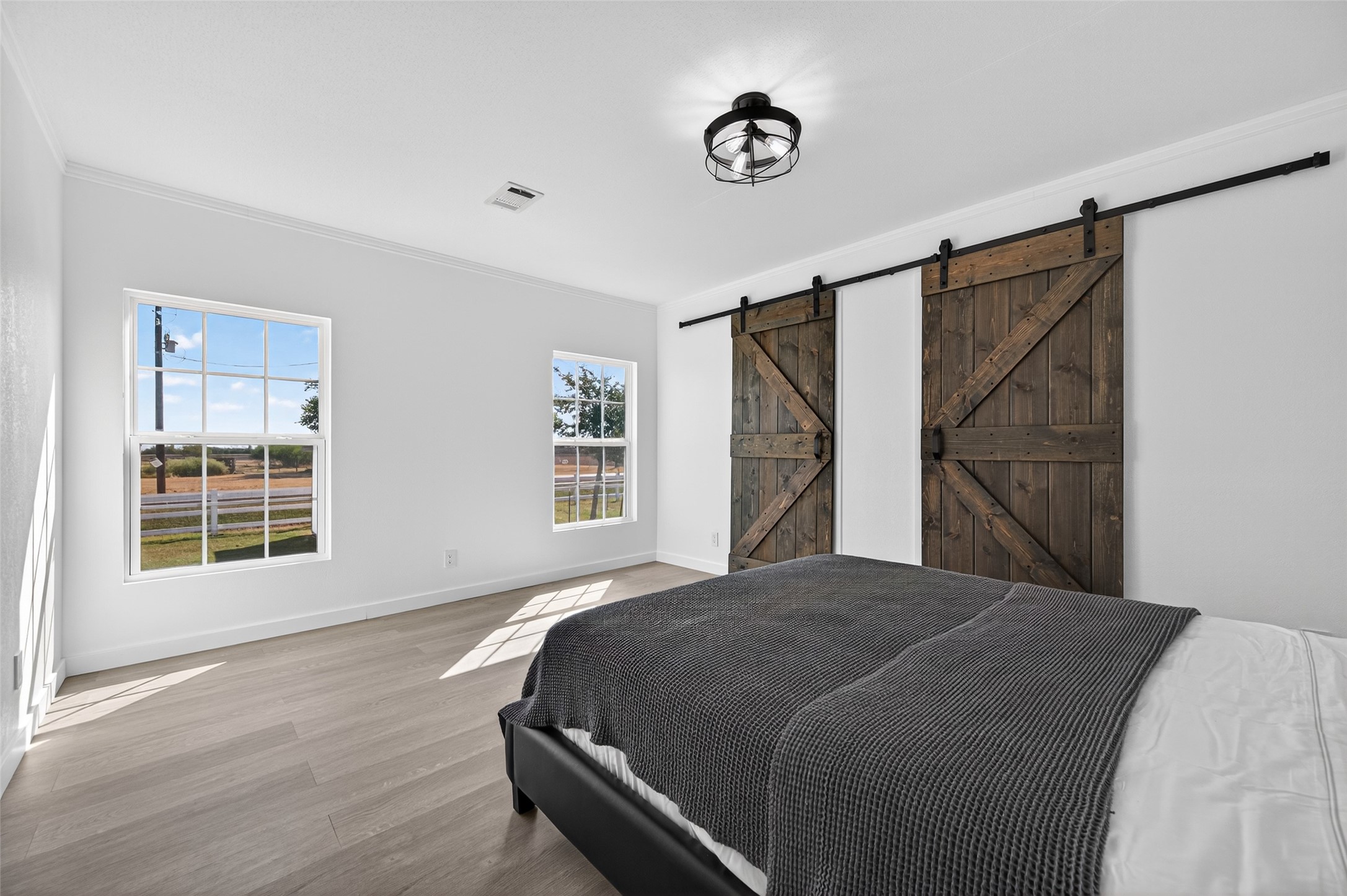 805 Williams Road East Bernard, TX 77435 - Photo 22 of 47 Spacious bedroom featuring rustic sliding barn doors, modern lighting, and windows overlooking open countryside.