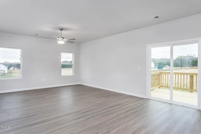 an empty room with wooden floor chandelier fan and windows