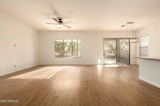 an empty room with wooden floor chandelier fan and windows