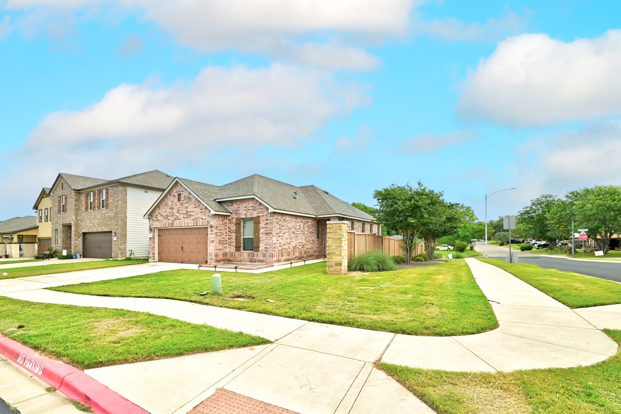 1621 Dragonfly Loop Bastrop, TX 78602 - Photo 2 of 27 Brick exterior home featuring an attached two-car garage, manicured lawn, and mature landscaping