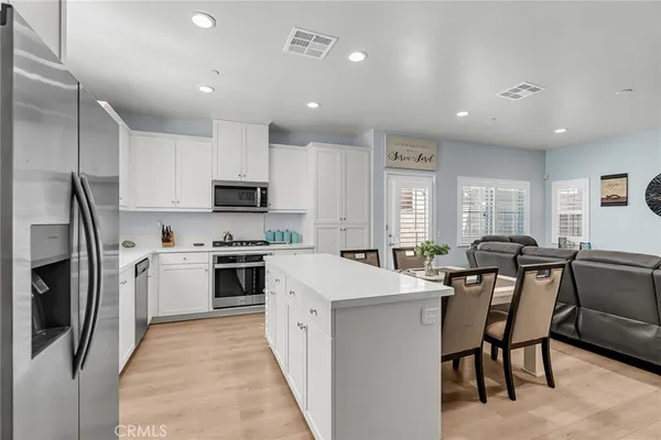 a kitchen with stainless steel appliances granite countertop a stove top oven a sink a refrigerator a dining table and chairs with wooden floor