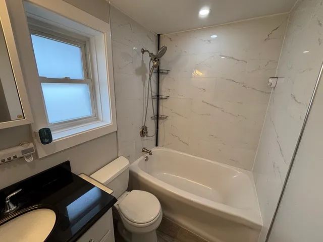 a bathroom with a granite countertop bathtub shower sink vanity and toilet
