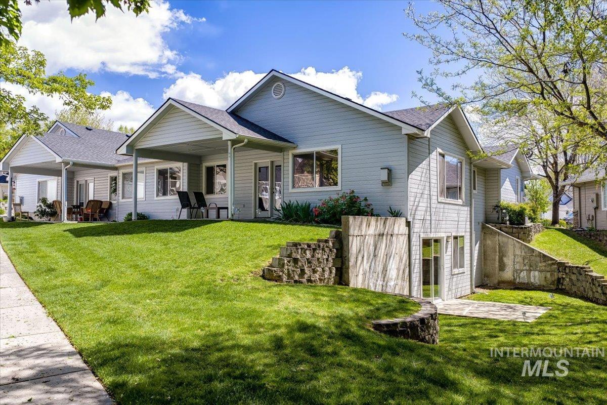 725 North Eagle Road Eagle, ID 83616 - Photo 35 of 45 Exterior featuring light blue siding, a covered patio, a walk-out lower level with glass door access, stone retaining walls, and a sloped, grassed yard