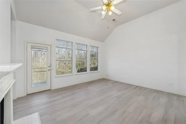 an empty room with wooden floor fan and windows