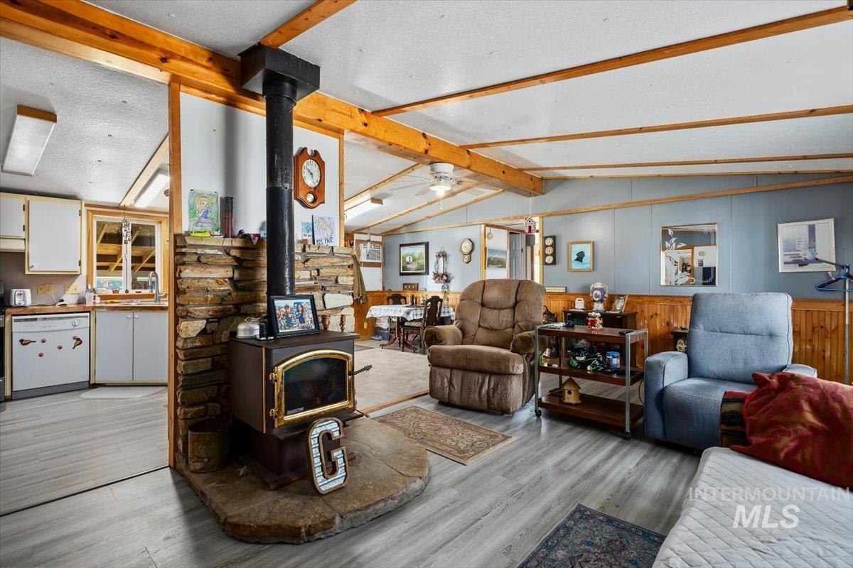 102 Willow Creek Road Fairfield, ID 83327 - Photo 6 of 32 Living area with a wood stove, a ceiling fan, beam ceiling, and light wood-style flooring