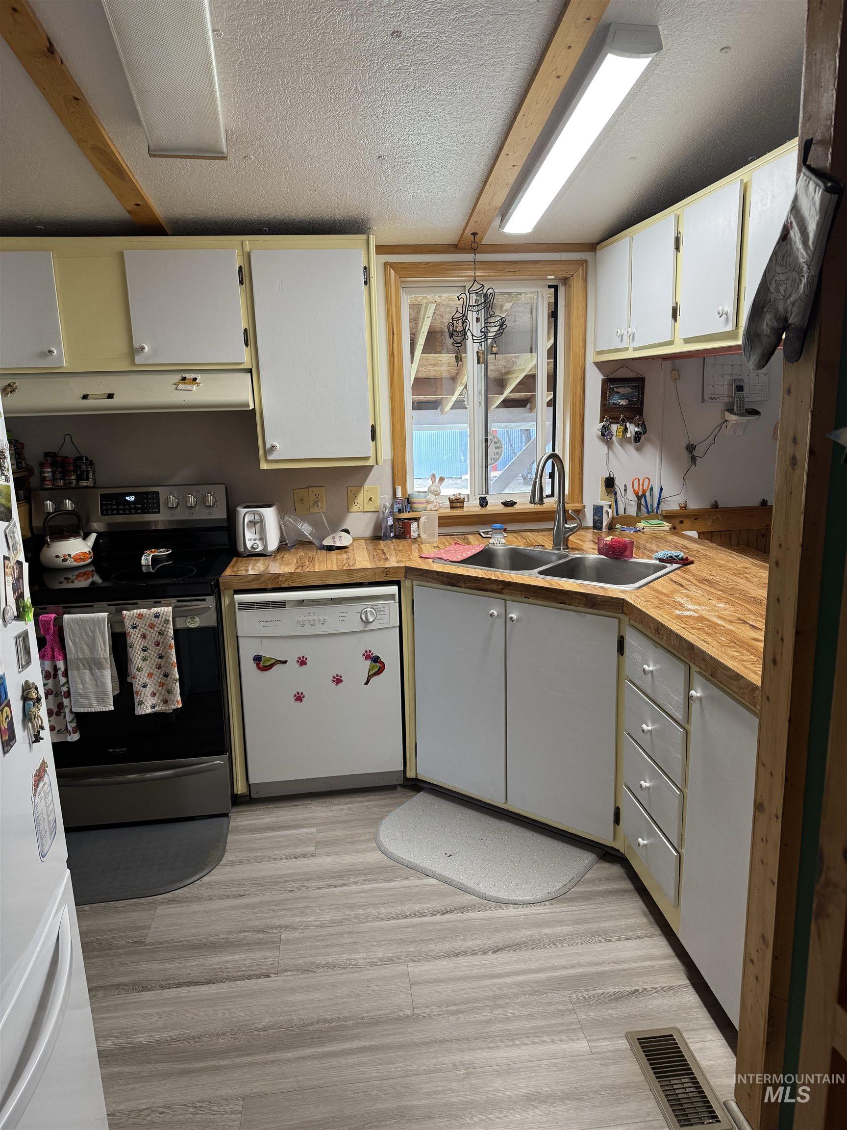 102 Willow Creek Road Fairfield, ID 83327 - Photo 7 of 40 Kitchen with white appliances, light countertops, a textured ceiling, white cabinetry, and light wood-style flooring