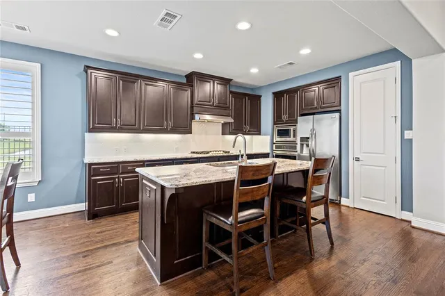 a kitchen with kitchen island granite countertop wooden floors cabinets and stainless steel appliances