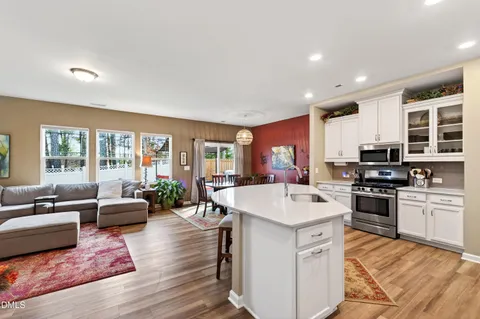 a open kitchen with stainless steel appliances granite countertop a stove top oven a sink dishwasher a dining table and chairs with wooden floor