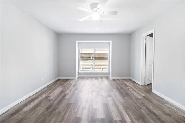 an empty room with wooden floor chandelier fan and windows
