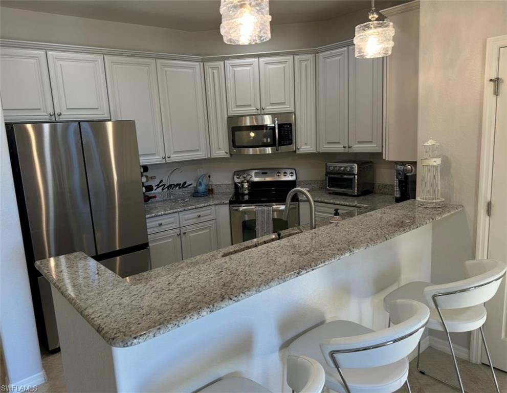 8997 Cambria Circle, Unit 2001 Naples, FL 34113 - Photo 5 of 42 Kitchen with a peninsula, a breakfast bar, light stone countertops, appliances with stainless steel finishes, and decorative light fixtures