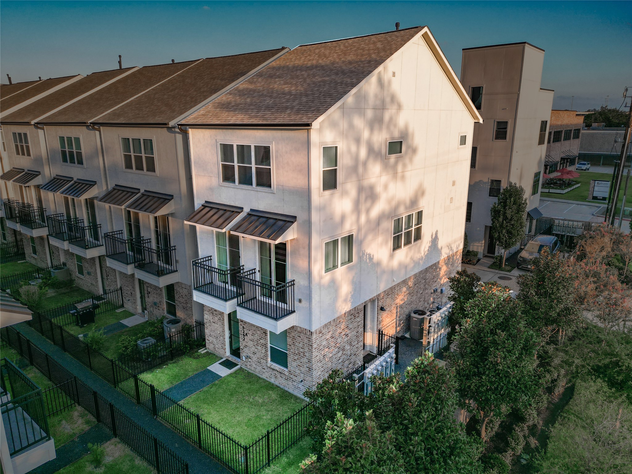 1262 North Post Oak Road, Unit A Houston, TX 77055 - Photo 48 of 50 An aerial view focusing on the front facade highlights the three-story brick and stucco exterior, dual second-floor balconies with dark metal awnings, and landscaped front yard area.