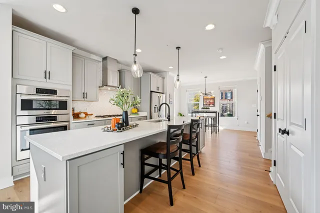 a kitchen with stainless steel appliances a refrigerator a sink a stove a dining table and chairs with wooden floor