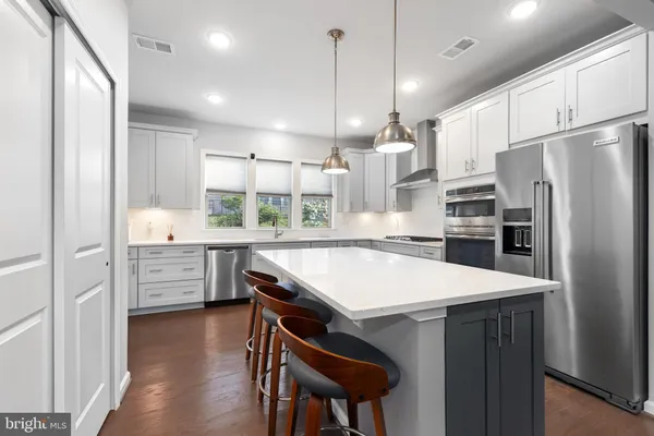 a kitchen with stainless steel appliances a stove a refrigerator a sink and white cabinets with wooden floors