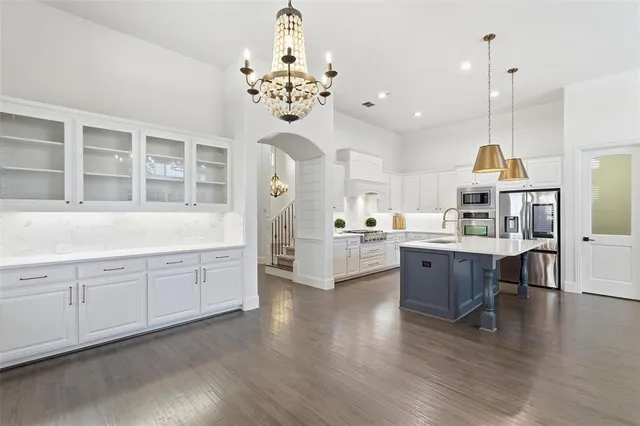 a large white kitchen with granite countertop a stove top oven a sink dishwasher and white cabinets with wooden floor