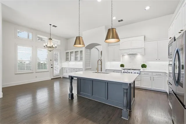 a kitchen with stainless steel appliances granite countertop a sink a stove a refrigerator and island with wooden floor