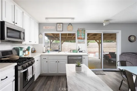 a kitchen with stainless steel appliances granite countertop a stove top oven a sink dishwasher a dining table and chairs with wooden floor