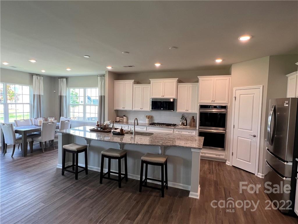 4027 Havenport Circle, Unit 121 Tega Cay, SC 29708 - Photo 8 of 24 a kitchen with stainless steel appliances granite countertop a stove a refrigerator a sink a dining table and chairs with wooden floor