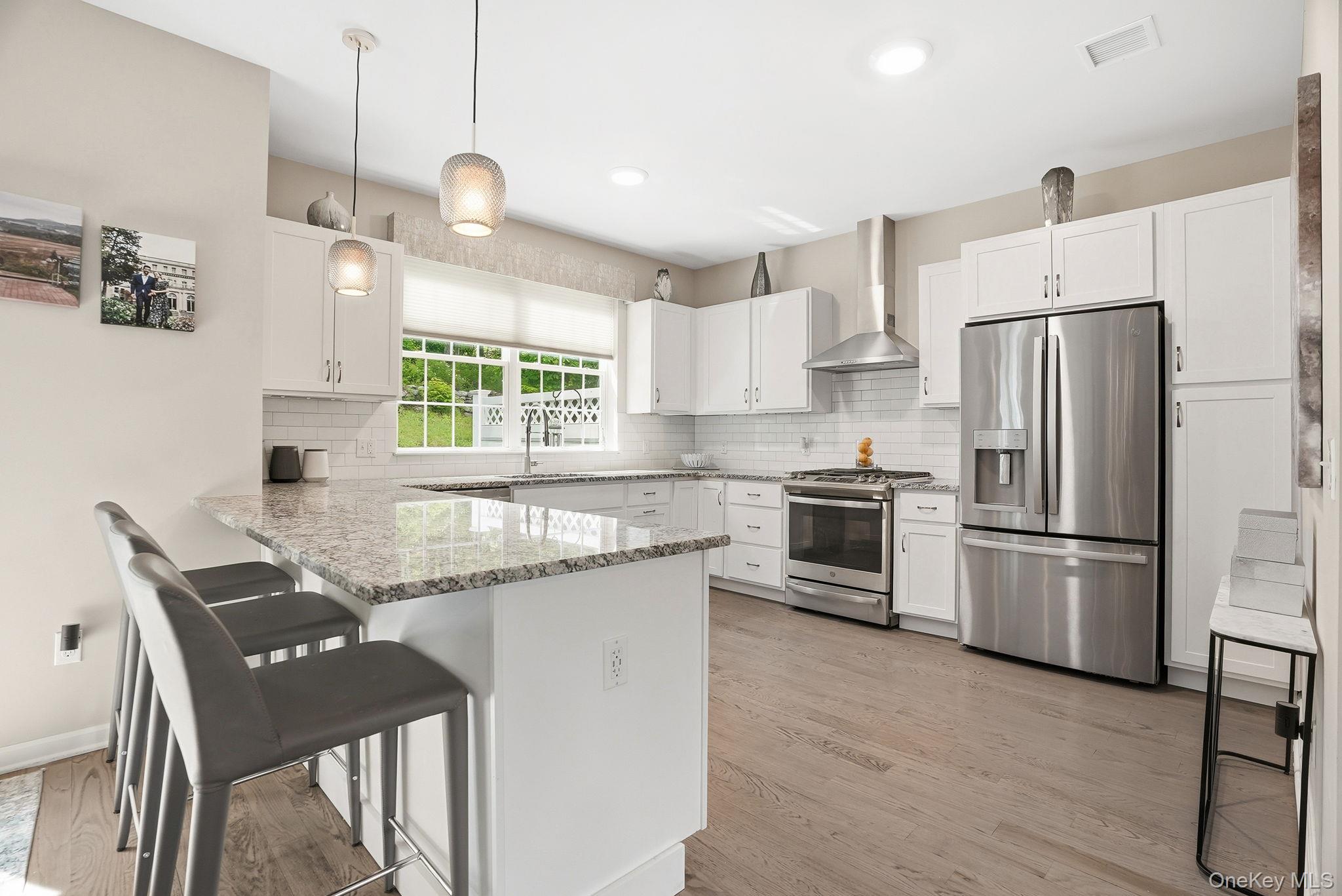 8 Muscoot River Road Granite Springs, NY 10527 - Photo 17 of 40 Modern kitchen featuring white cabinetry, light-toned wood-finish flooring, stainless steel appliances, a white subway tile backsplash, and a large central island with a light-colored countertop