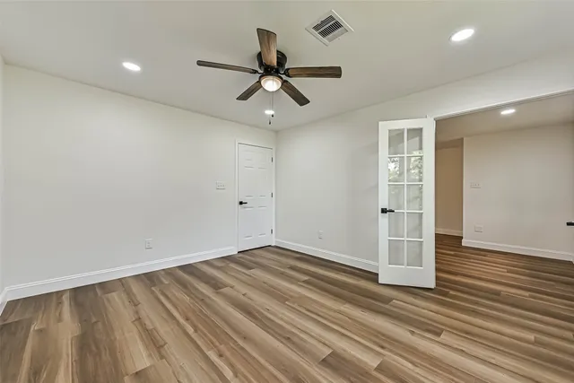 an empty room with wooden floor ceiling fan and windows