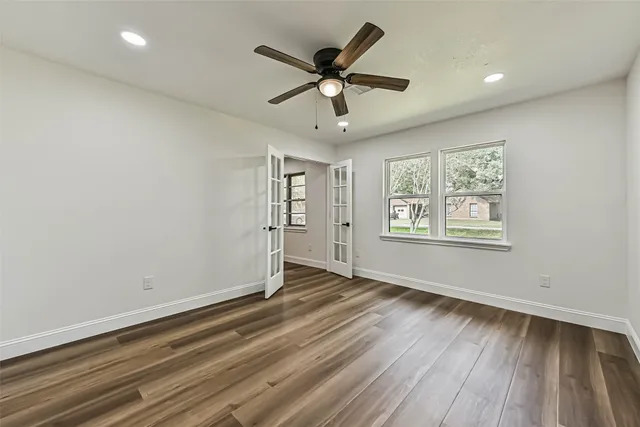 an empty room with wooden floor ceiling fan and windows