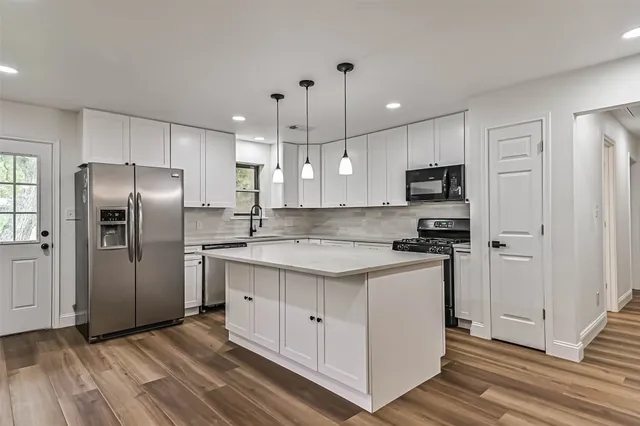 a kitchen with stainless steel appliances granite countertop a refrigerator a sink a stove and oven a wooden floor