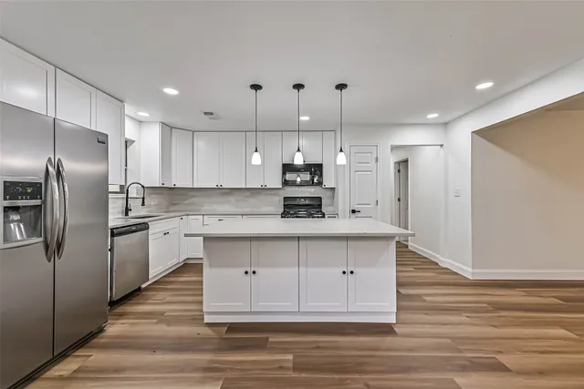 a kitchen with stainless steel appliances kitchen island granite countertop a refrigerator a sink dishwasher a stove and white cabinets with wooden floor