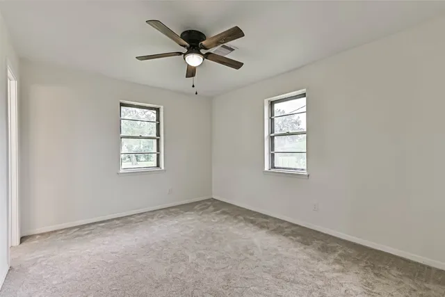 an empty room with windows and ceiling fan