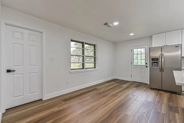 an empty room with wooden floor cabinet and windows