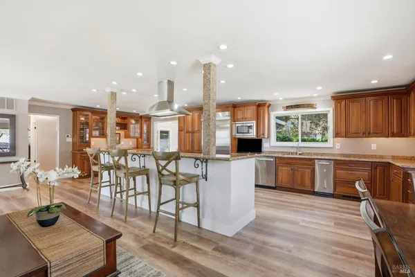 a kitchen with stainless steel appliances kitchen island granite countertop a table chairs and a wooden cabinets