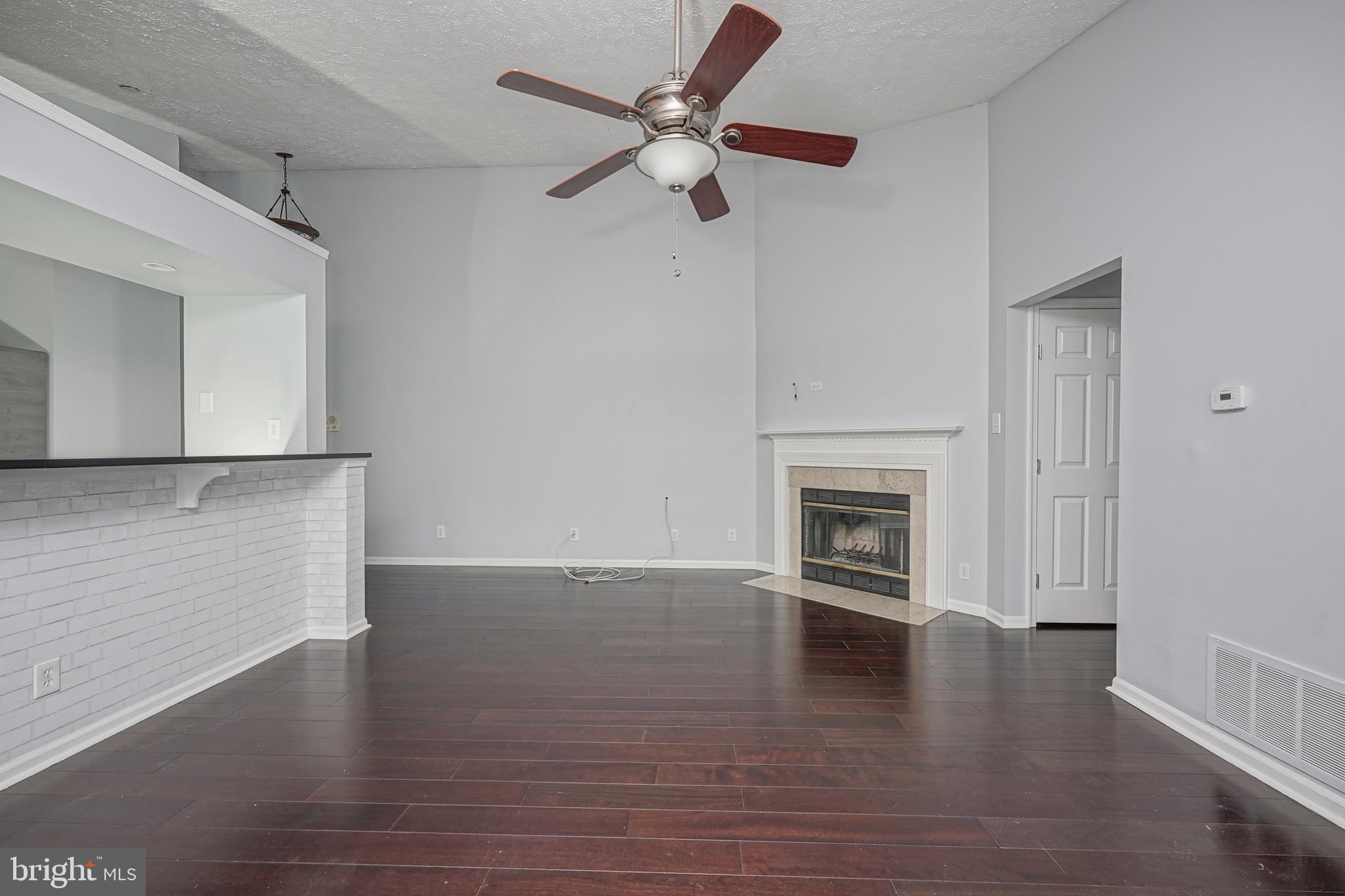 84 Eldon Way Marlton, NJ 08053 - Photo 4 of 27 an empty room with wooden floor a ceiling fan a kitchen view and a fireplace