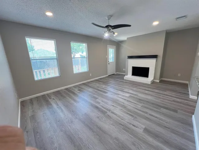 an empty room with wooden floor fireplace and windows