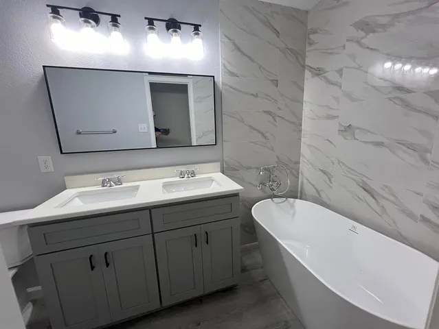 a bathroom with a double vanity sink and mirror with bathtub