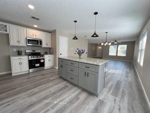 a kitchen with stainless steel appliances kitchen island granite countertop a stove a sink and a wooden floors