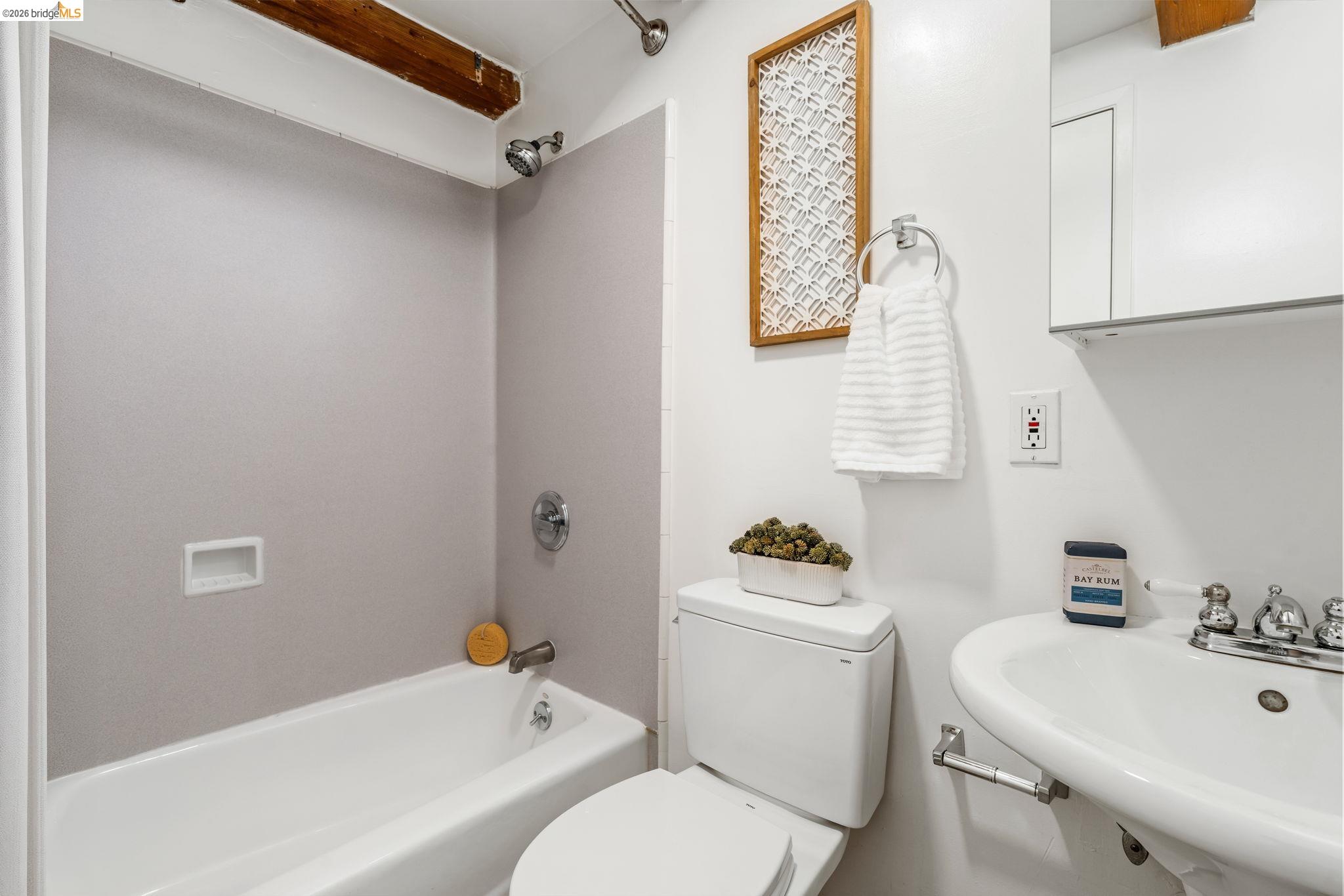 1920 Union Street, Unit 9 Oakland, CA 94607 - Photo 27 of 35 White ceramic bathtub with chrome fixtures, exposed wood ceiling beam, white pedestal sink with chrome faucet, and wall-mounted medicine cabinet