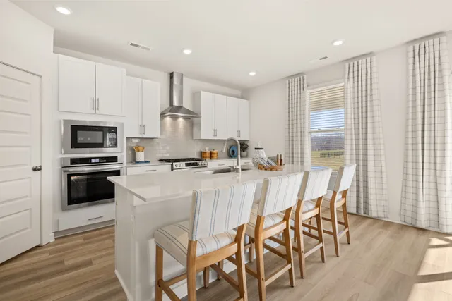 a kitchen with stainless steel appliances kitchen island granite countertop a stove a sink a microwave a refrigerator and white cabinets with wooden floor