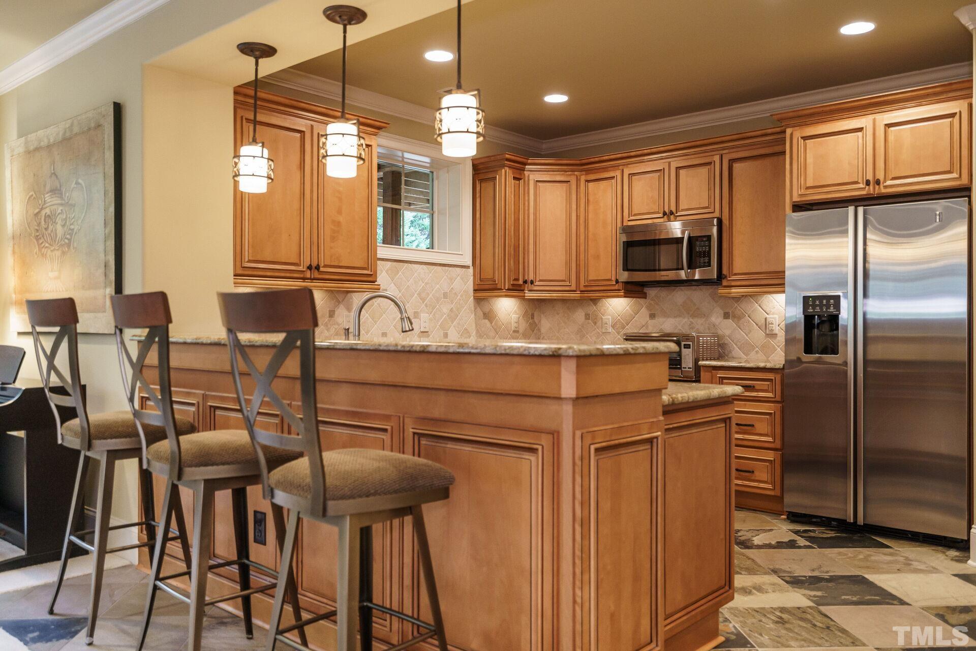 8313 Rue Cassini Court Raleigh, NC 27615 - Photo 45 of 74 a kitchen with stainless steel appliances kitchen island granite countertop a table chairs and a refrigerator