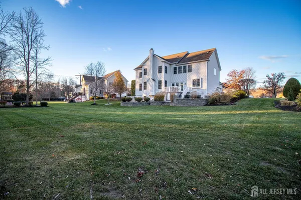 a view of a white house in front of a big yard with plants and large trees