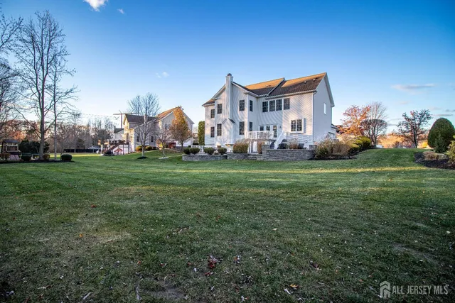 a view of a white house in front of a big yard with plants and large trees