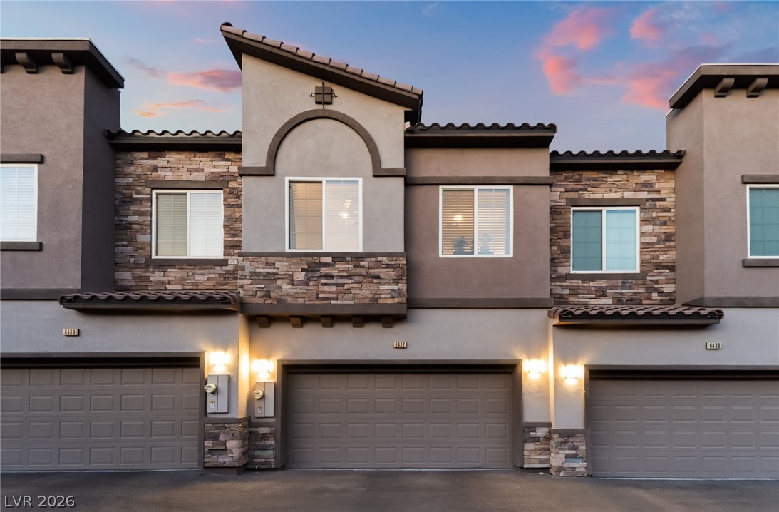 6432 Spring Jog Street Las Vegas, NV 89166 - Photo 51 of 61 A striking modern facade with stone accents and inviting garage lighting at dusk.