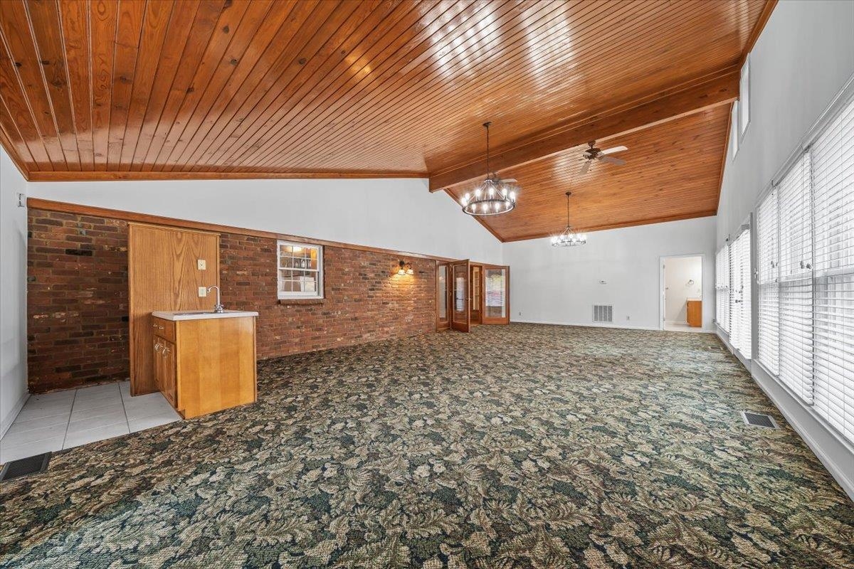 102 Linden Street Grand Junction, TN 38039 - Photo 18 of 37 Unfurnished living room with brick wall, light colored carpet, a chandelier, ceiling fan, and a wooden ceiling with exposed beams