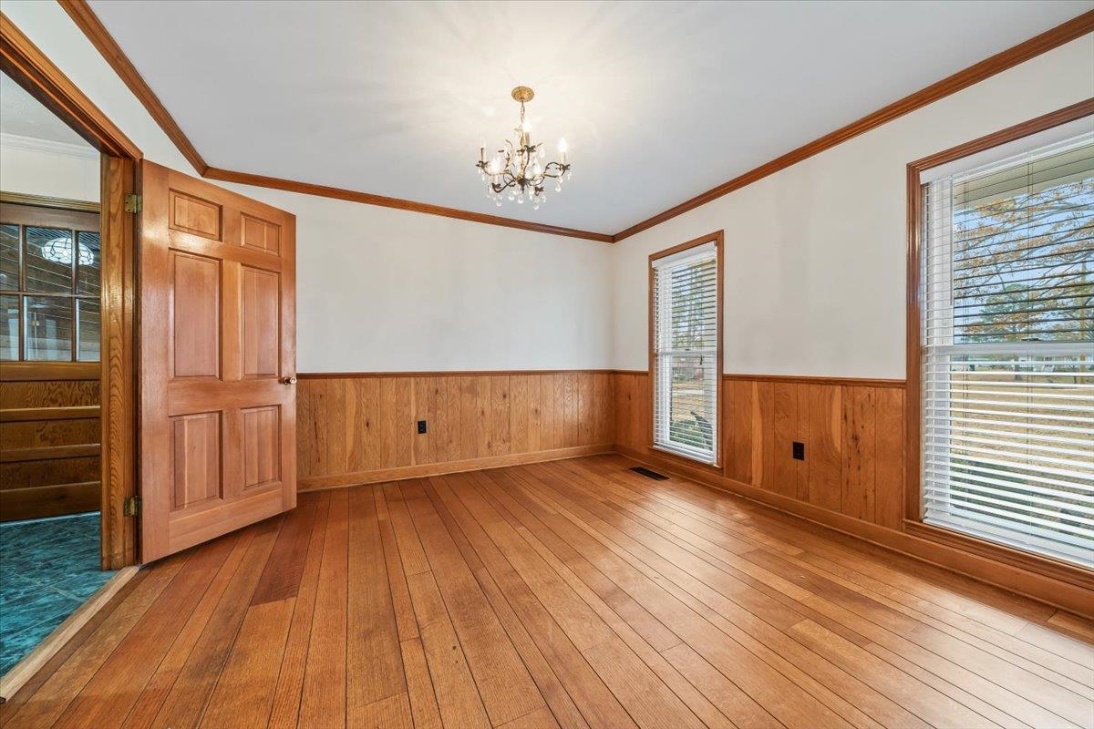 102 Linden Street Grand Junction, TN 38039 - Photo 9 of 37 Empty room featuring light wood-type flooring, ornamental molding, a chandelier, a wainscoted wall, and wooden walls