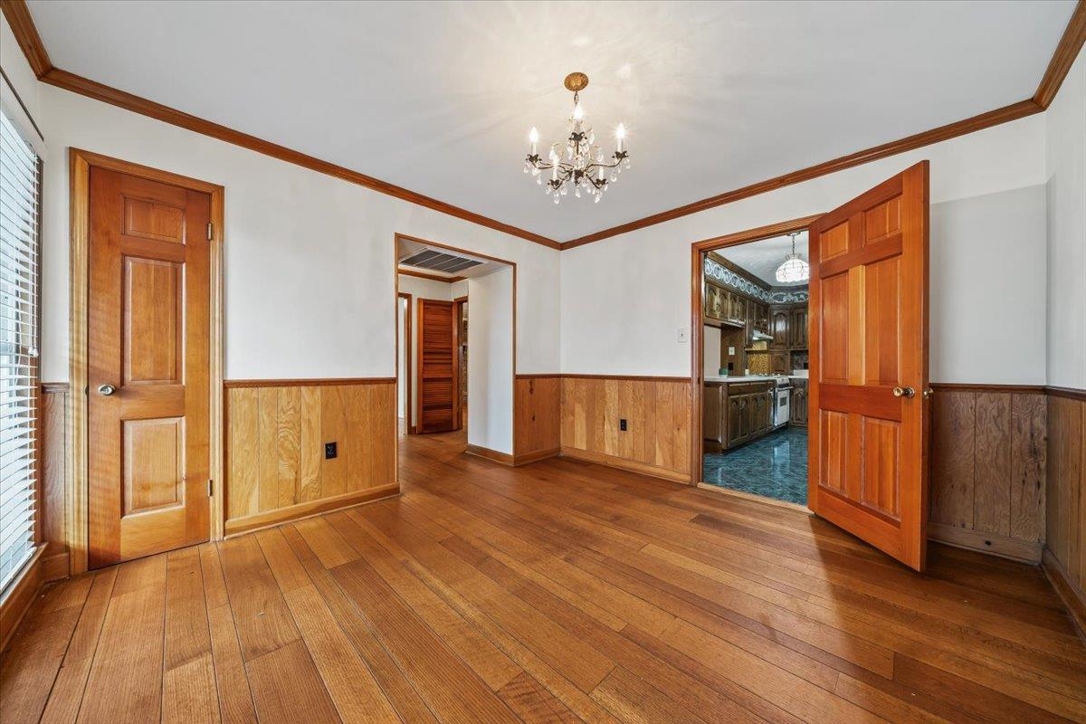 102 Linden Street Grand Junction, TN 38039 - Photo 10 of 37 Empty room with dark wood-type flooring, ornamental molding, a chandelier, wainscoting, and wooden walls