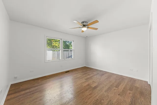 an empty room with wooden floor ceiling fan and windows